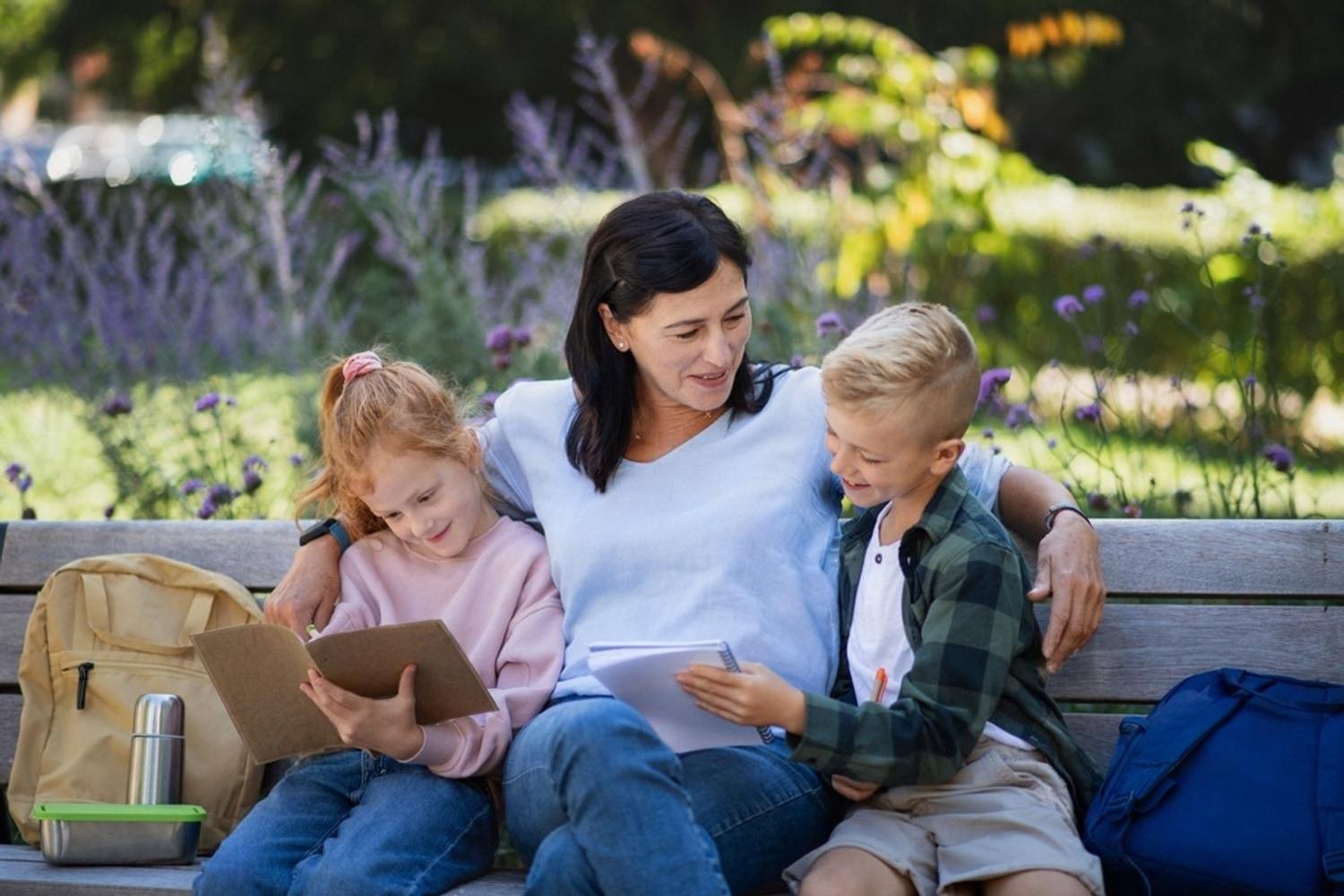Mother reading with her son and daughter on a park bench after school